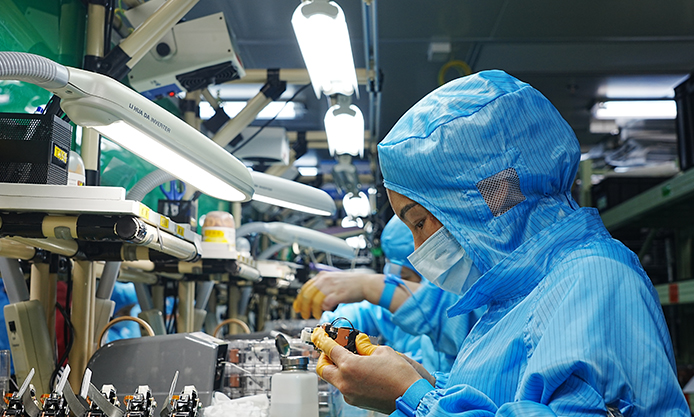 TOUMEI worker in protective clothing handling a component at a production workstation