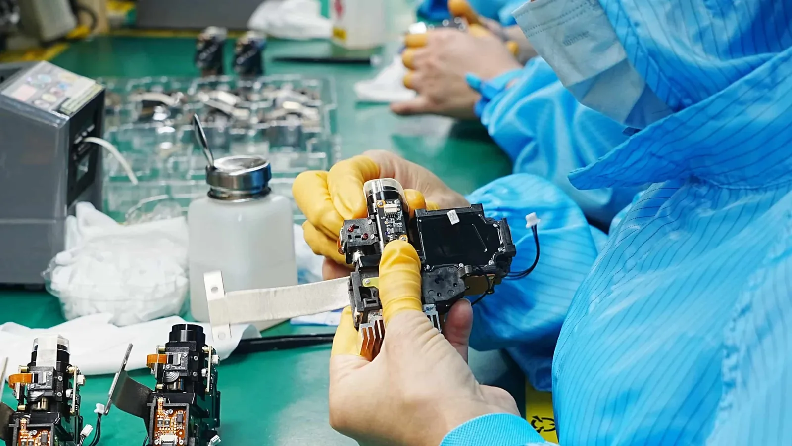 2026 Projector Assortment Planning: 10 China-Linked Product Examples for OEM and Wholesale Buyers 2 Gloved worker holding a projector optical assembly with visible lens and circuit boards at a TOUMEI workbench